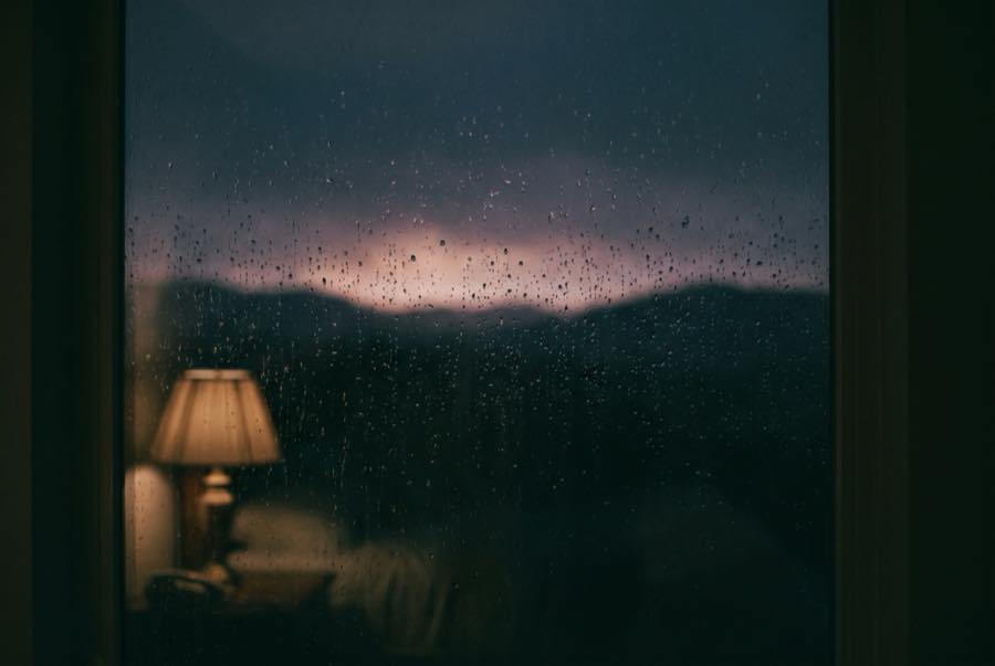 Rain on a dark bedroom window at night, a faint storm glow far away on the horizon